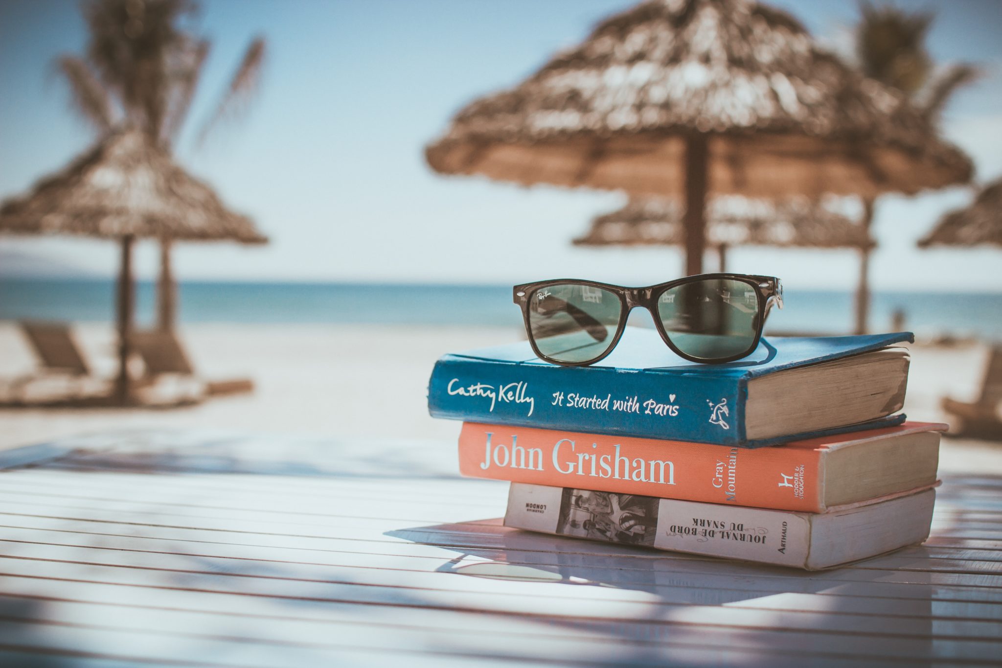 Książki i okulary leżące na stole na plaży w Bułgarii w słoneczny dzień, z widokiem na parasole, plażę i morze