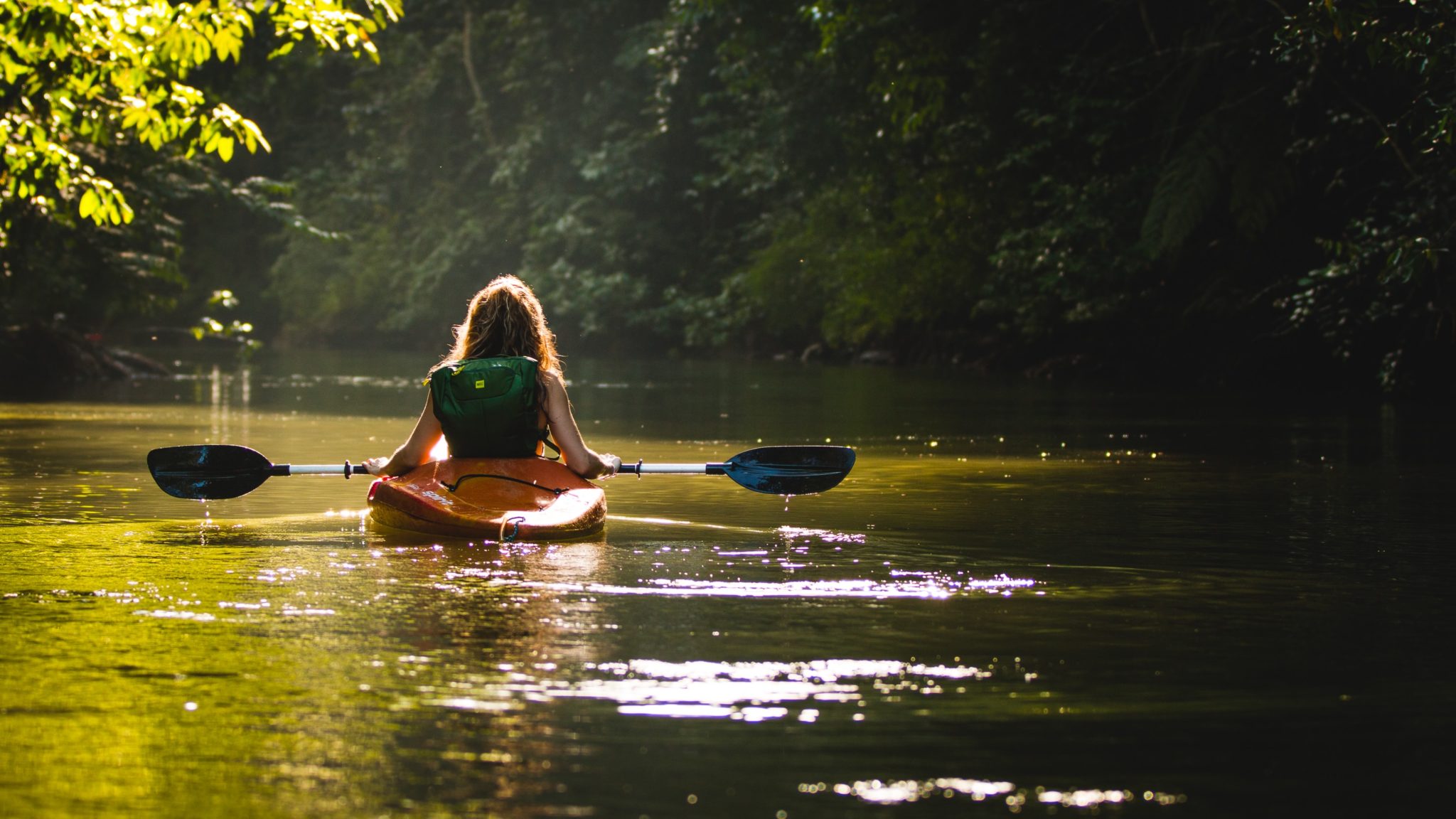Dziewczyna w kajaku spływająca rzeką w środku lasu