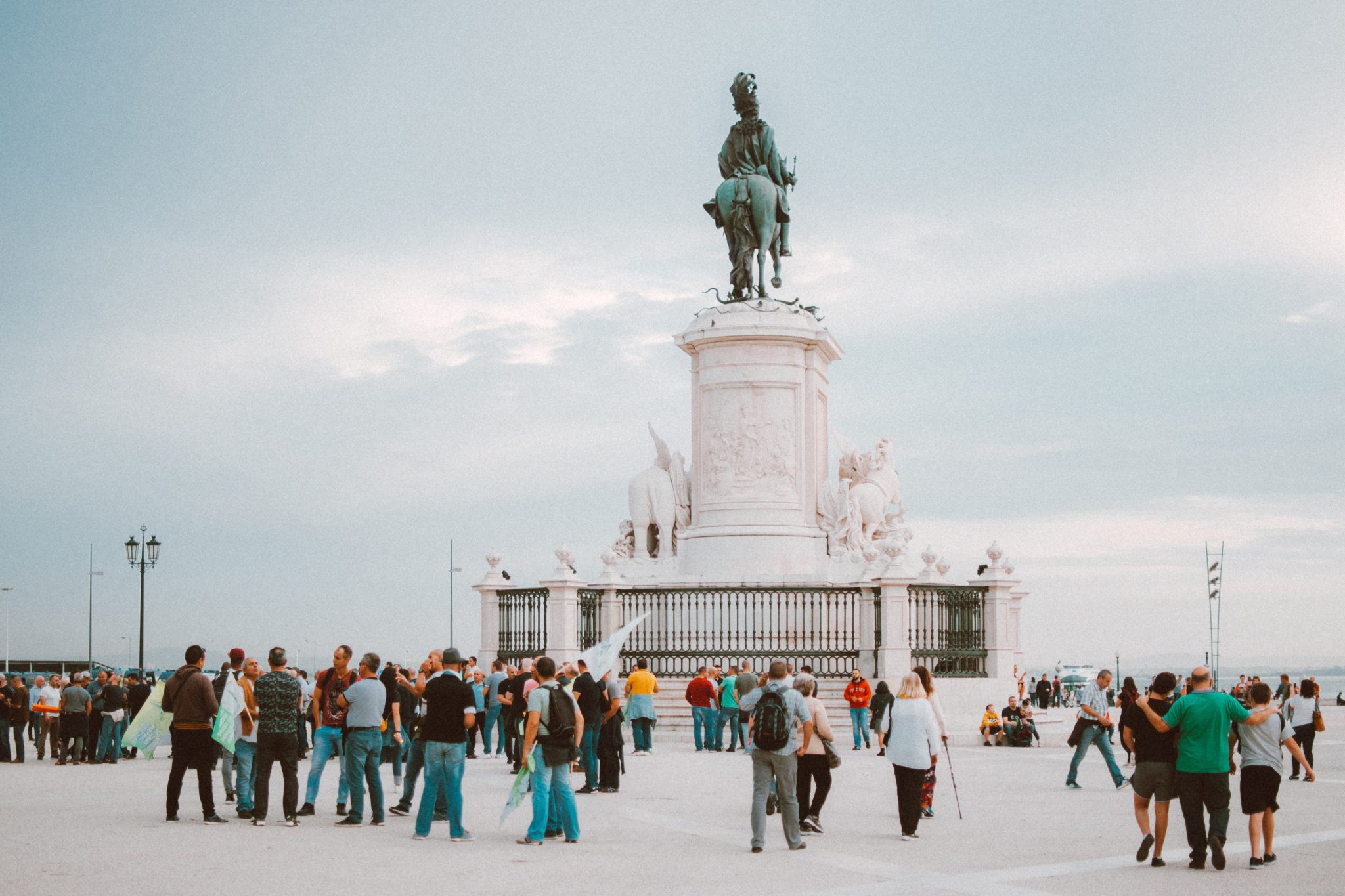 Duży plac handlowy na którym mieści się pomnik Józefa I na koniu. Wokół pomnika duża grupa zwiedzających Lizbonę turystów.