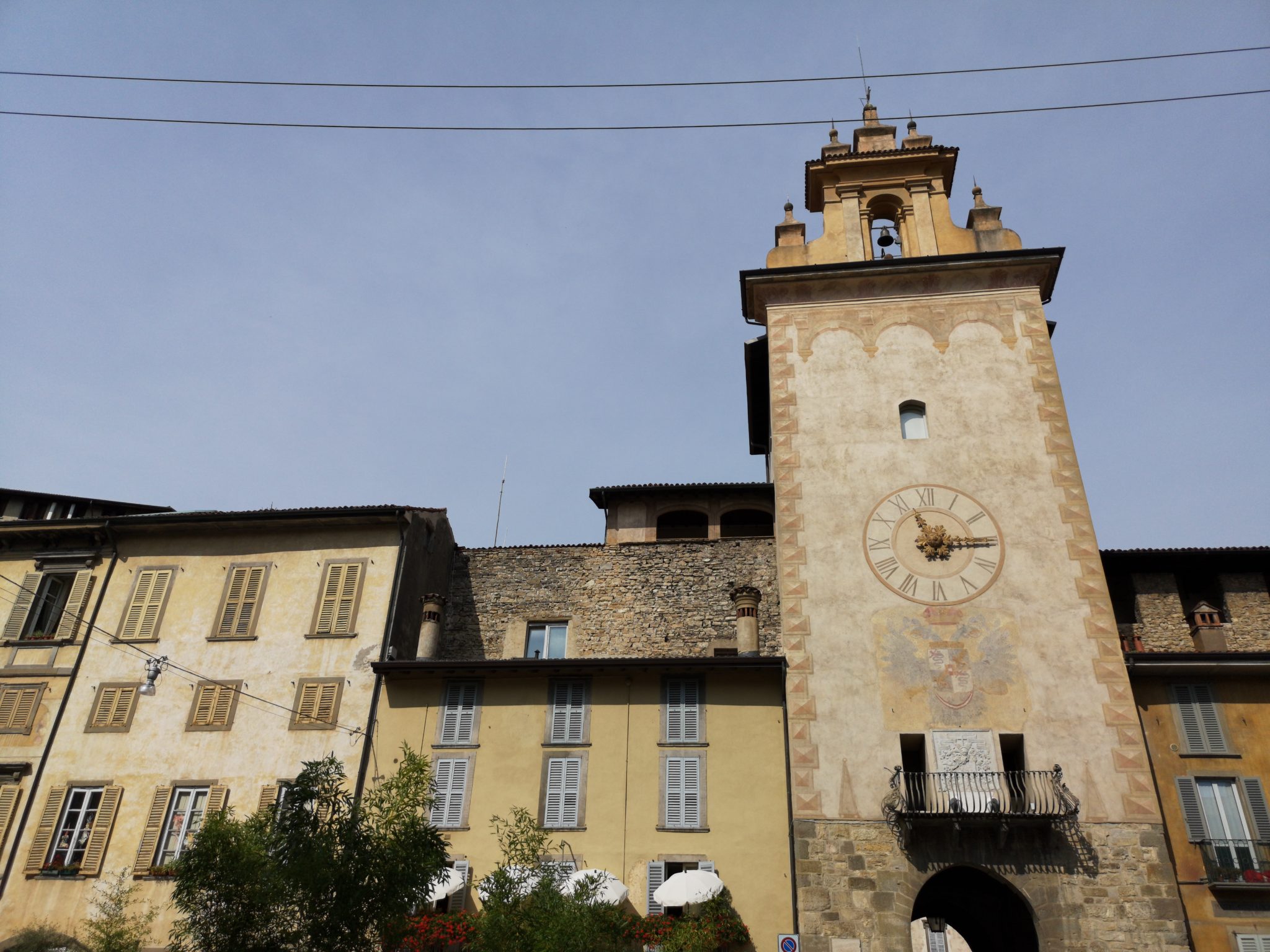 Ciąg budynków zbudowanych we włoskim stylu, stara wieża z zegarem na tle niebieskiego nieba