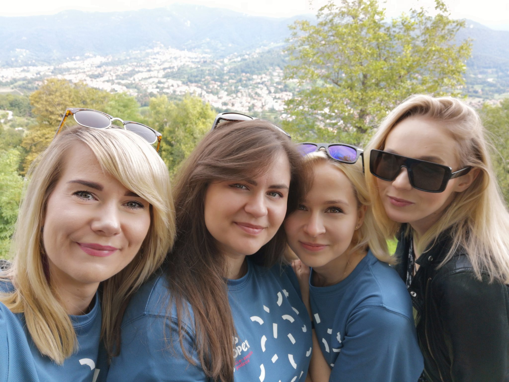 Cztery dziewczyny przyjaciółki pozujące do zdjęcia na wzgórzu w Bergamo, za nimi piękne widoki na okoliczne miasteczka i góry