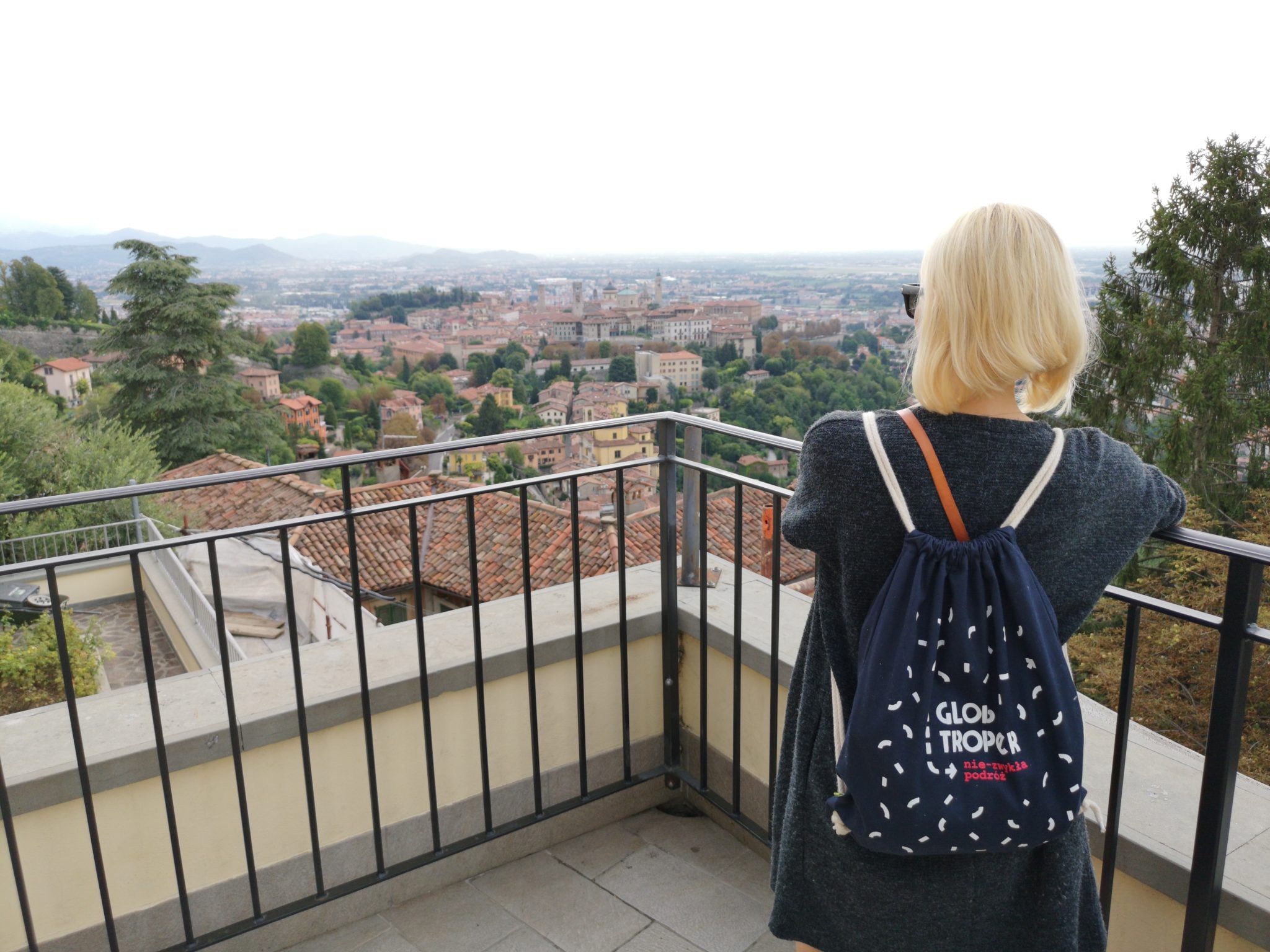 Dziewczyna z plecakiem stojąca na tarasie widokowym i obserwująca piękną panoramę miasta Bergamo we Włoszech