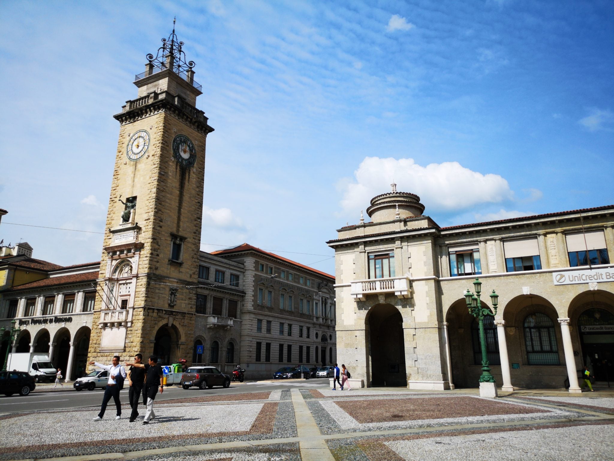 Plac w mieście Bergamo z Wieżą Poległych - Torre dei Caduti - oraz z arkadowym budynkiem, w słoneczny dzień