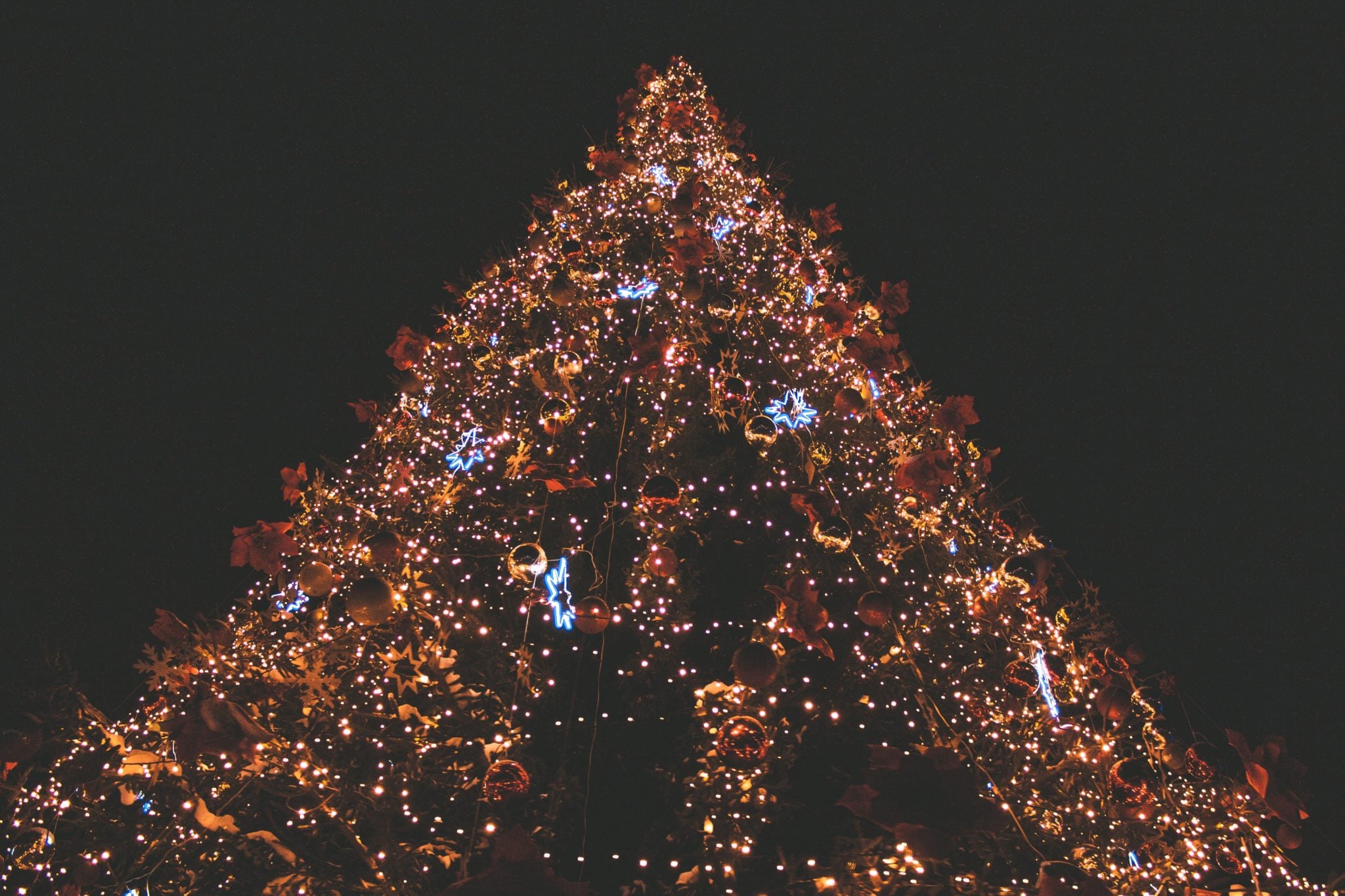 Duża choinka przyozdobiona lampkami choinkowymi, bombkami i ozdobami, stojąca na Jarmarku Bożonarodzeniowym