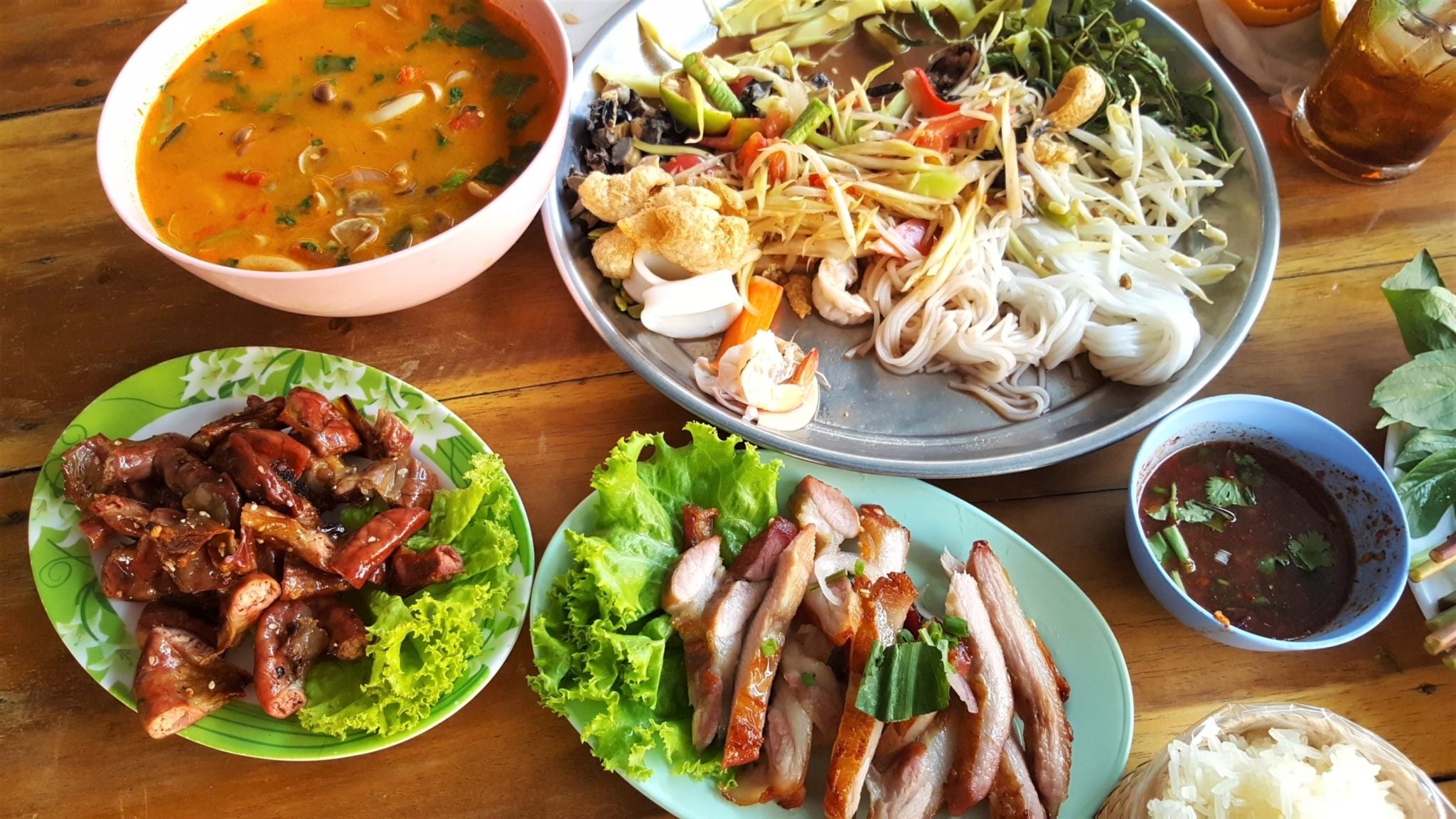 Na stole talerze wypełnione azjatyckim jedzeniem, noodle ryżowe, mięso, aromatyczne przyprawy i warzywa