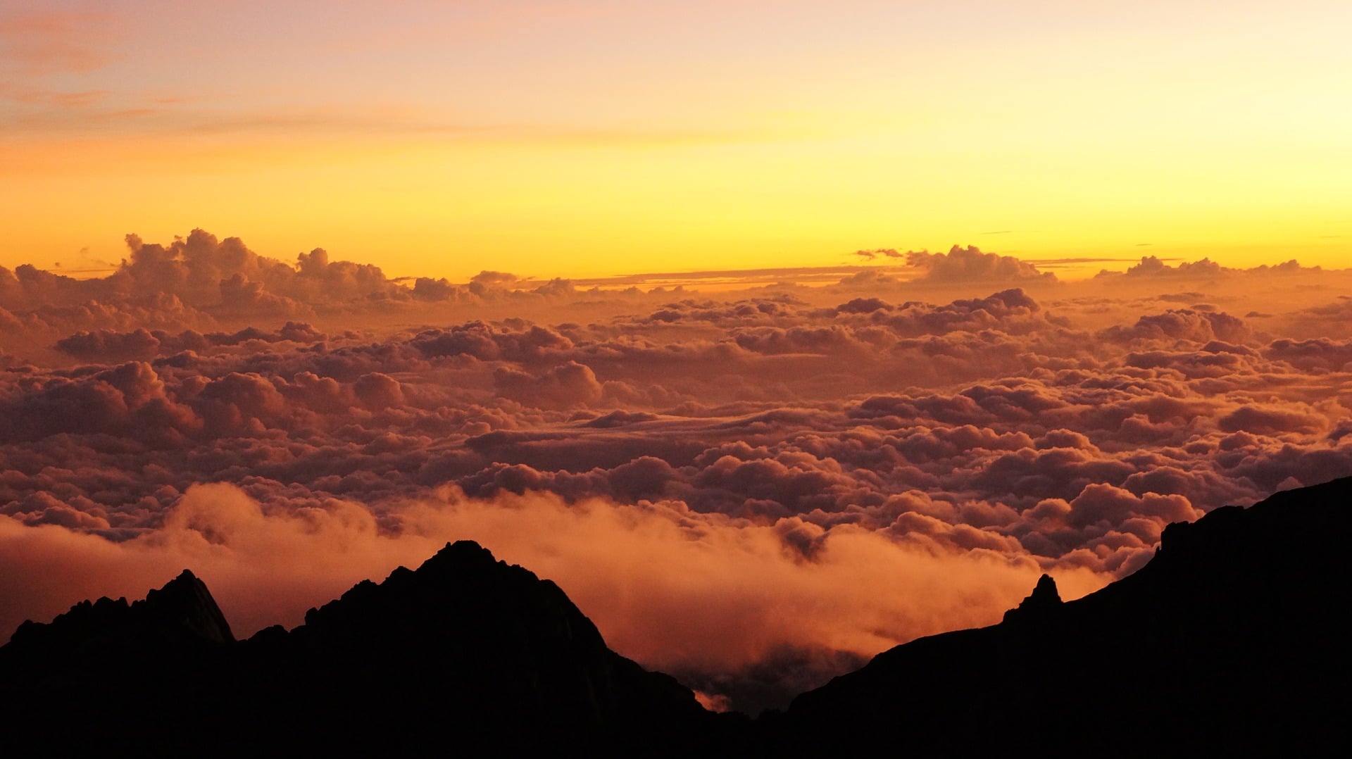 Wschodzące słońce koloruje szczyt najwyższej góry Malezji Kinabalu i chmury przybierają pomarańczowy kolor