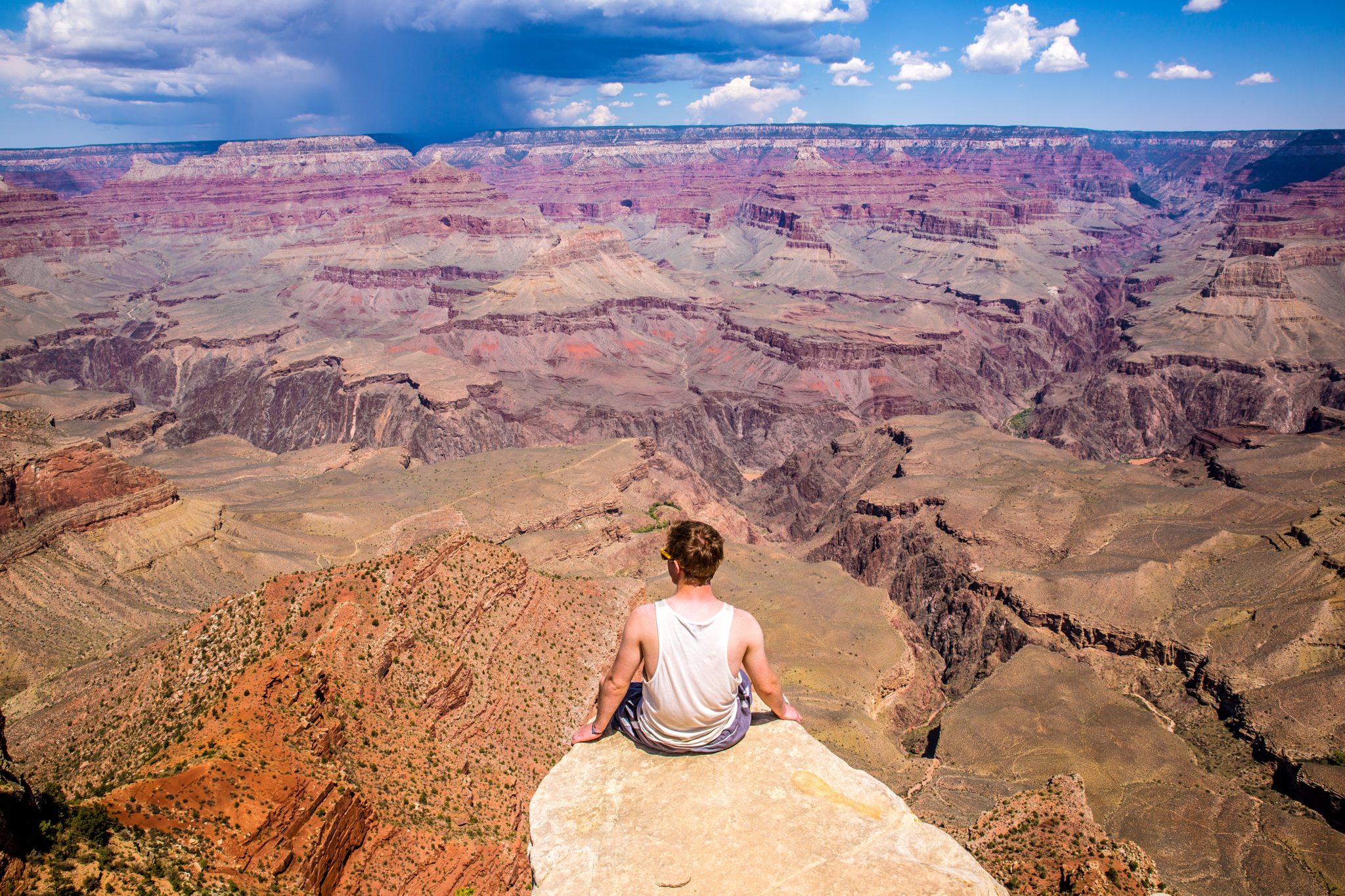 Mężczyzna siedzący na brzegu głazu, w tle widok na piękny Wielki Kanion Kolorado w Arizonie w USA w słoneczny dzień