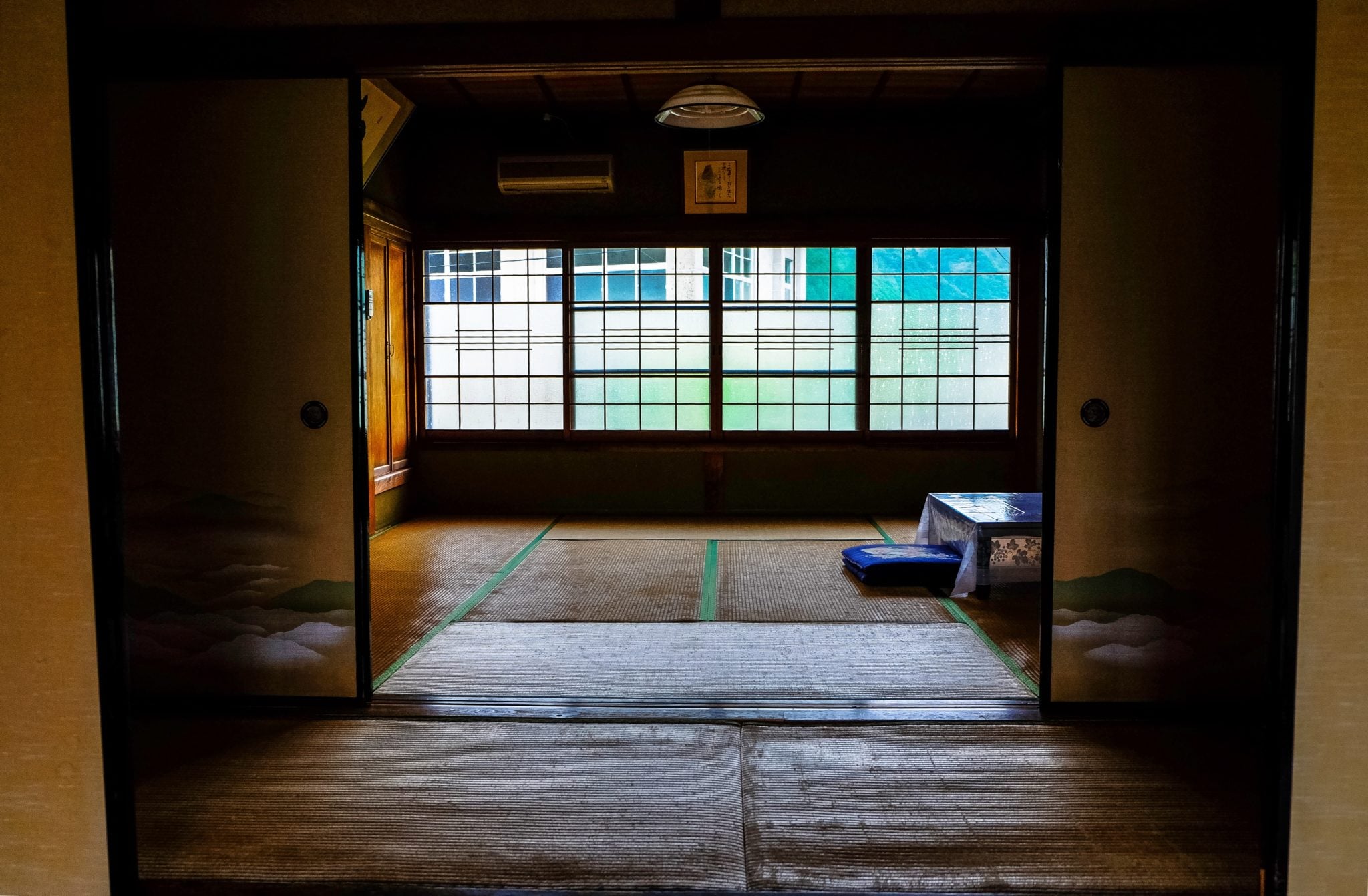 Pokój w Japonii wyłożony tradycyjnymi matami tatami, stolik do siedzenia i siedzisko na podłodze, drzwi do pokoju są otwarte i pięknie zdobione sztuką japońską