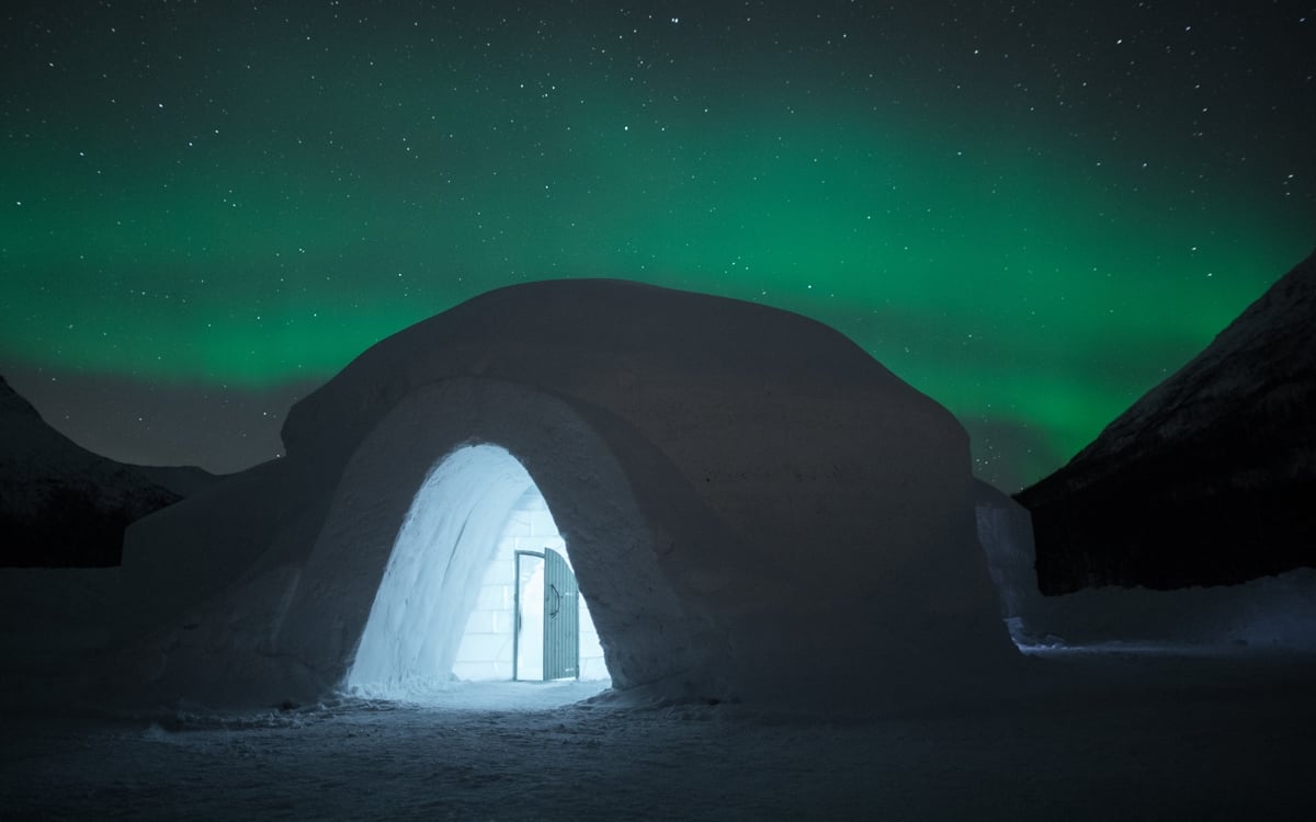Widok na lodowy hotel z zewnątrz, wygląda jak igloo, noc rozświetlona zielonymi światłami zorzy polarnej