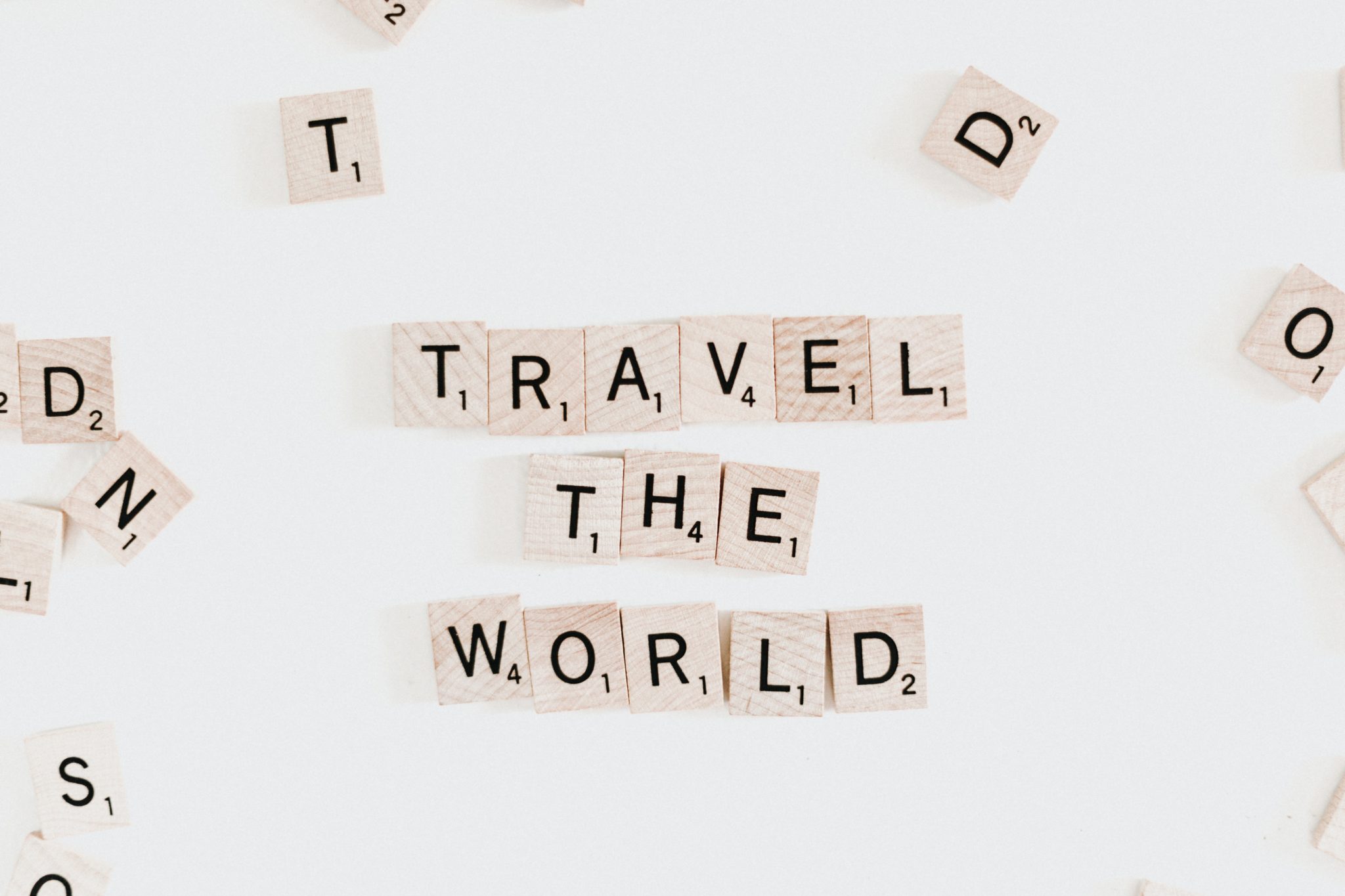 Rozsypane scrabble na białym stole, ułożone w napis podróżuj, travel the world