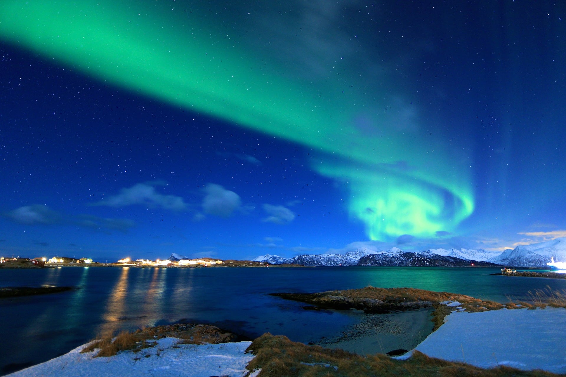 Widok na morze, ośnieżone góry, fiordy i tańcząca na niebie kolorowa zorza polarna